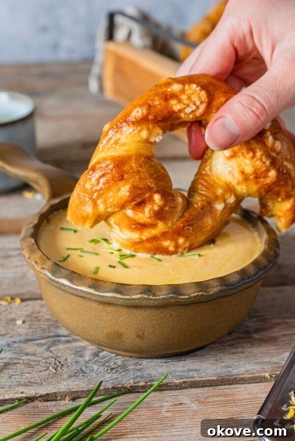 A small bowl of cheese with a soft pretzel being dipped into the cheese.