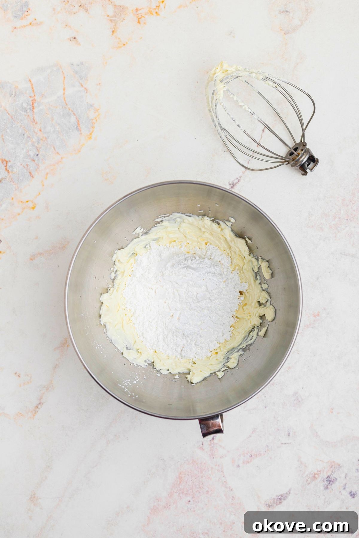 Creamy Oreo Dessert Dip for Parties and Snacks 5 Powdered sugar being added to cream cheese in a silver mixing bowl.