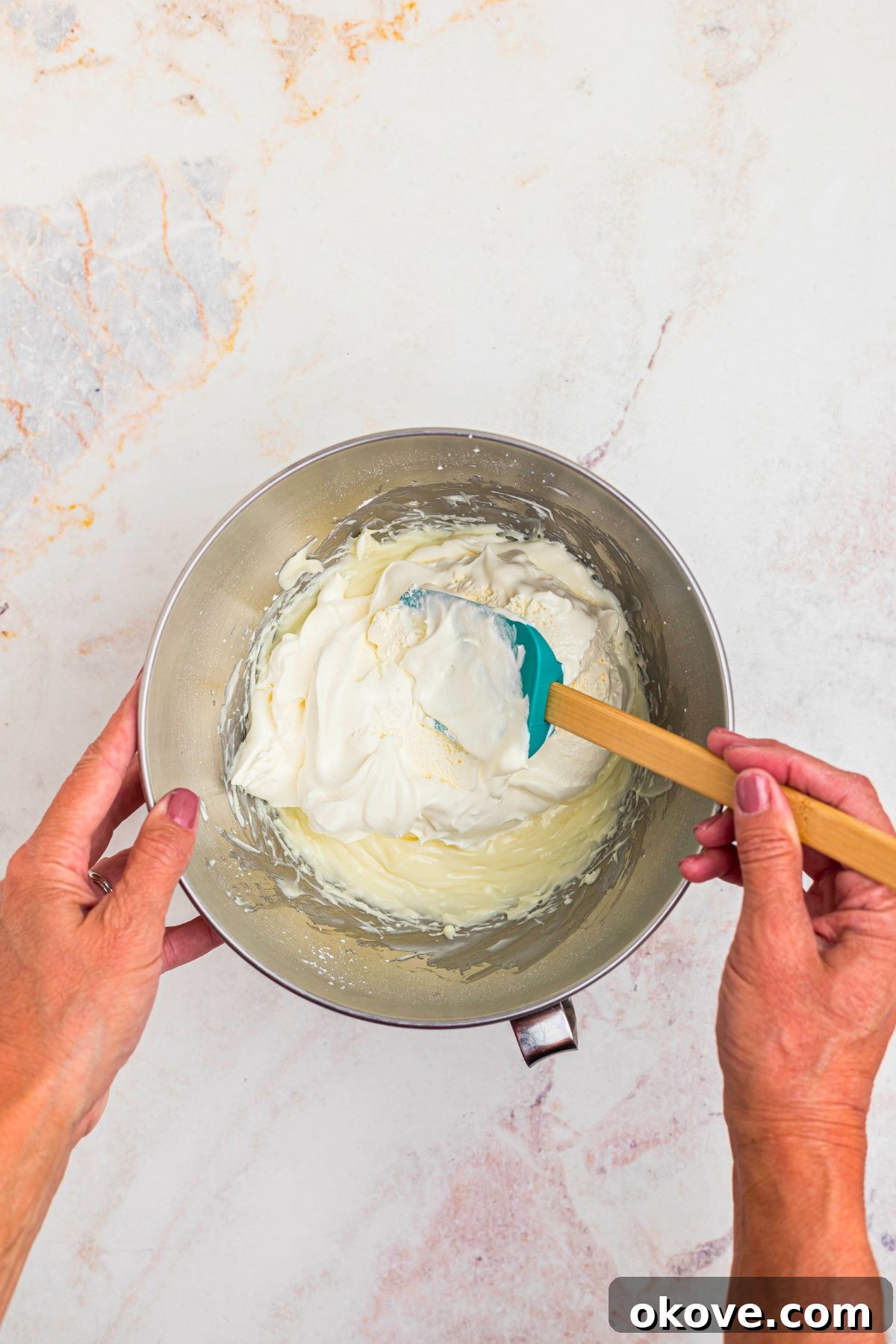 Creamy Oreo Dessert Dip for Parties and Snacks 6 Cool whip being mixed in to cream cheese mixture in a silver mixing bowl, with a spatula.