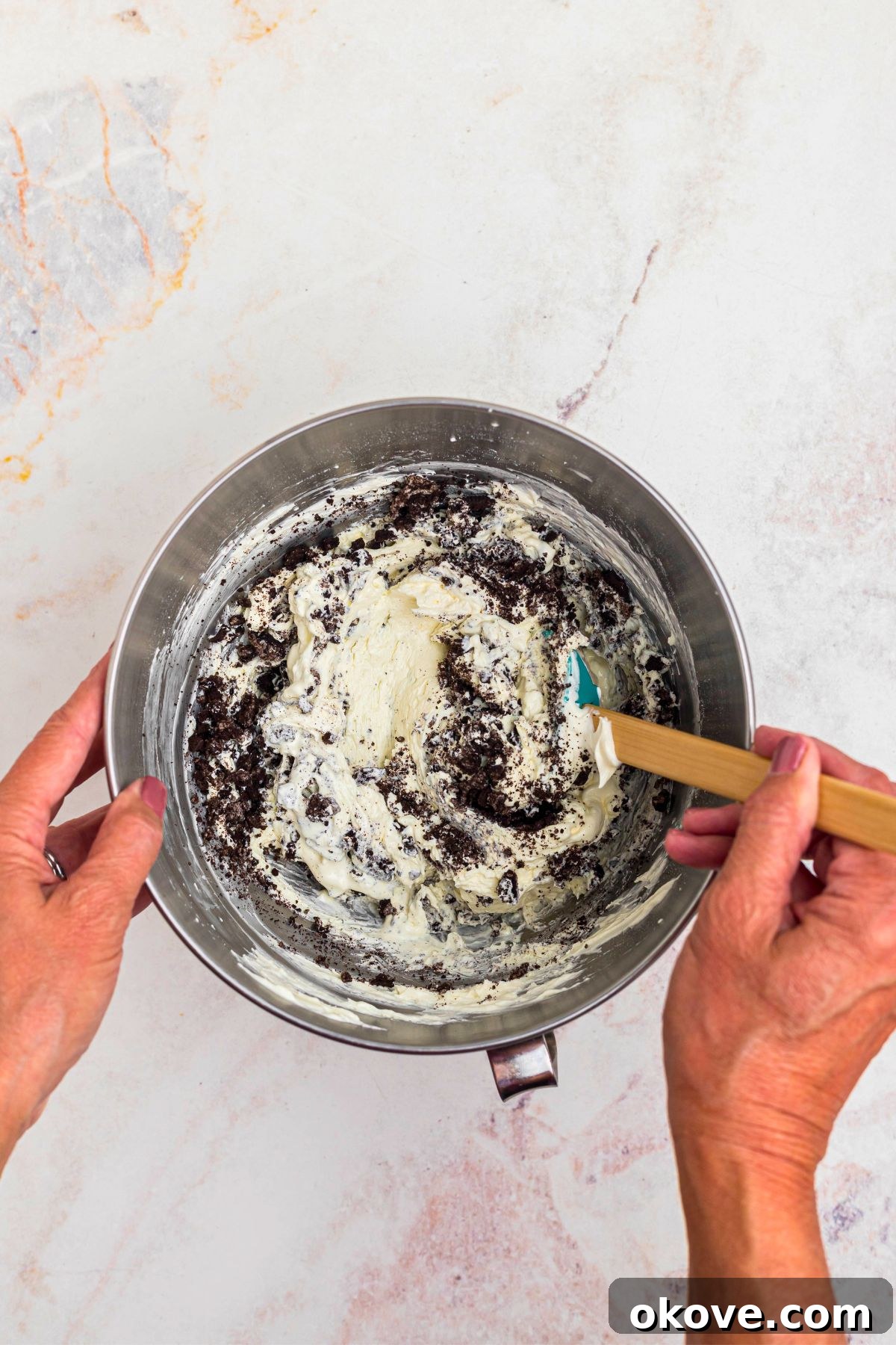Creamy Oreo Dessert Dip for Parties and Snacks 7 Crushed Oreos being stirred into cream cheese mixture in a silver mixing bowl.