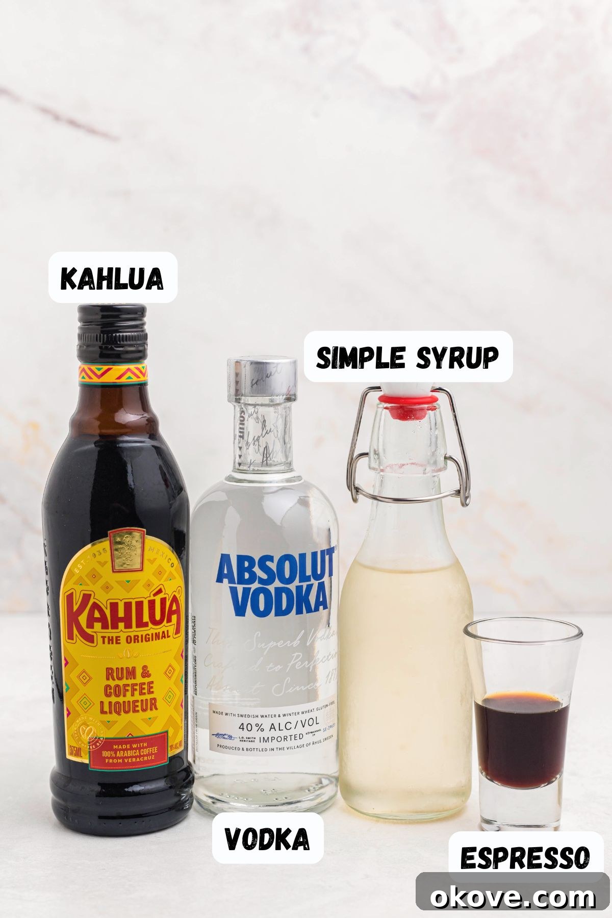 Espresso Martini Cocktail Recipe 3 Kahlua, vodka, simple syrup, and espresso, on a white marble table, labeled.