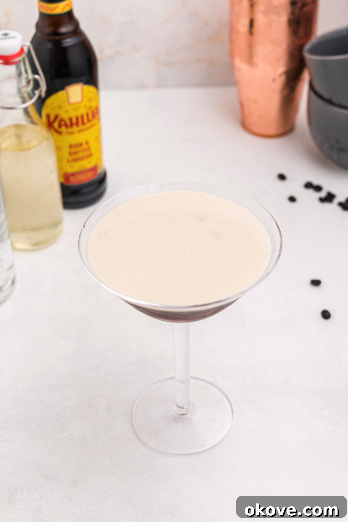 Espresso Martini Cocktail Recipe 5 Froth on top of an espresso and vodka mixture, in a martini glass, with coffee beans spread around the table.