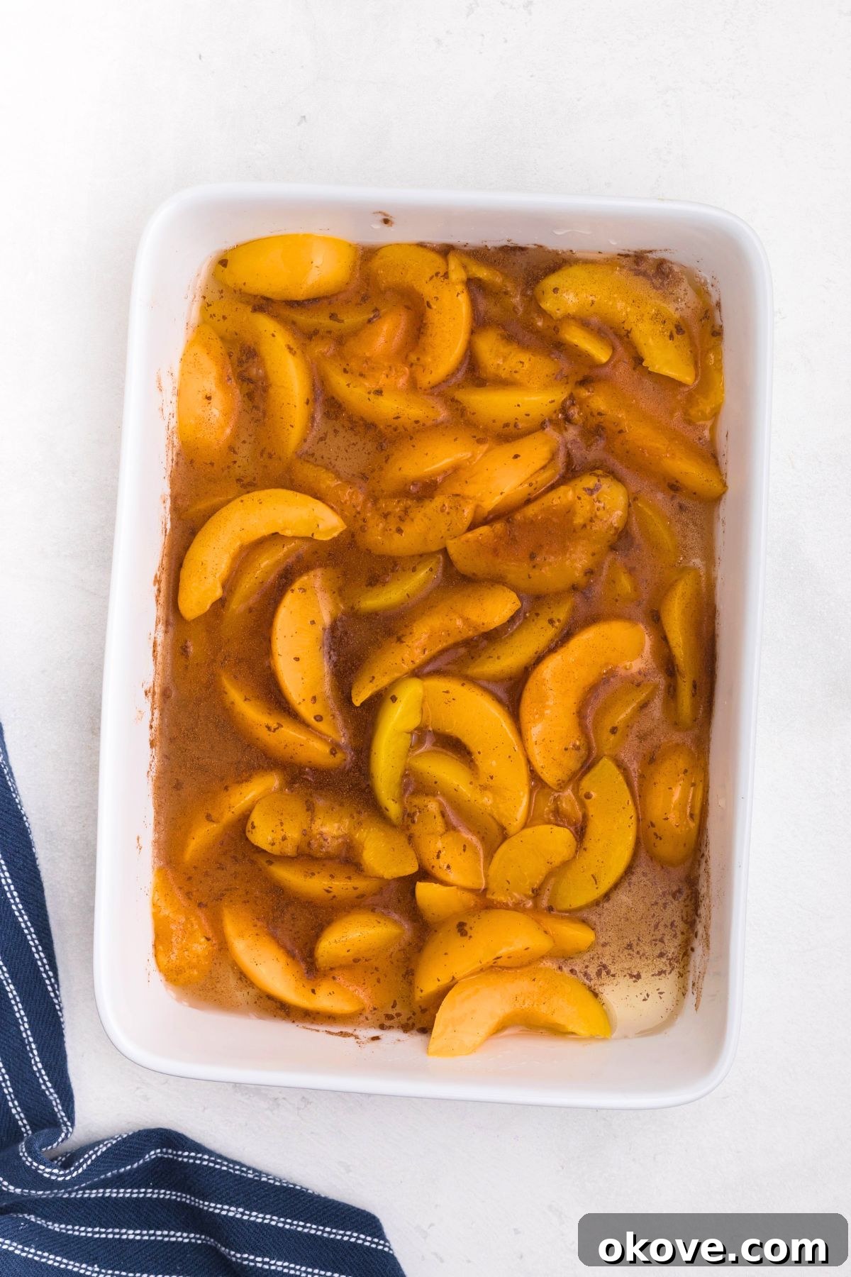 Irresistible Peach Dump Cake Recipe for Summer Desserts 4 White rectangular dish filled with peaches, mixed with cinnamon and vanilla.