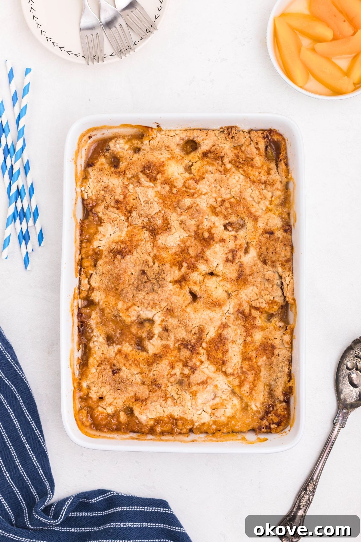 Irresistible Peach Dump Cake Recipe for Summer Desserts 7 Peaches in a white rectangle dish, covered in box cake mix, drizzled with melted butter, then baked until golden brown and bubbly.