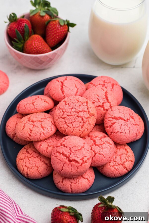 Classic Peanut Butter Blossom Cookies with Chocolate Kiss 10 Pink strawberry cake mix cookies stacked on a blue plate in front of glasses of milk and bowls of strawberries.