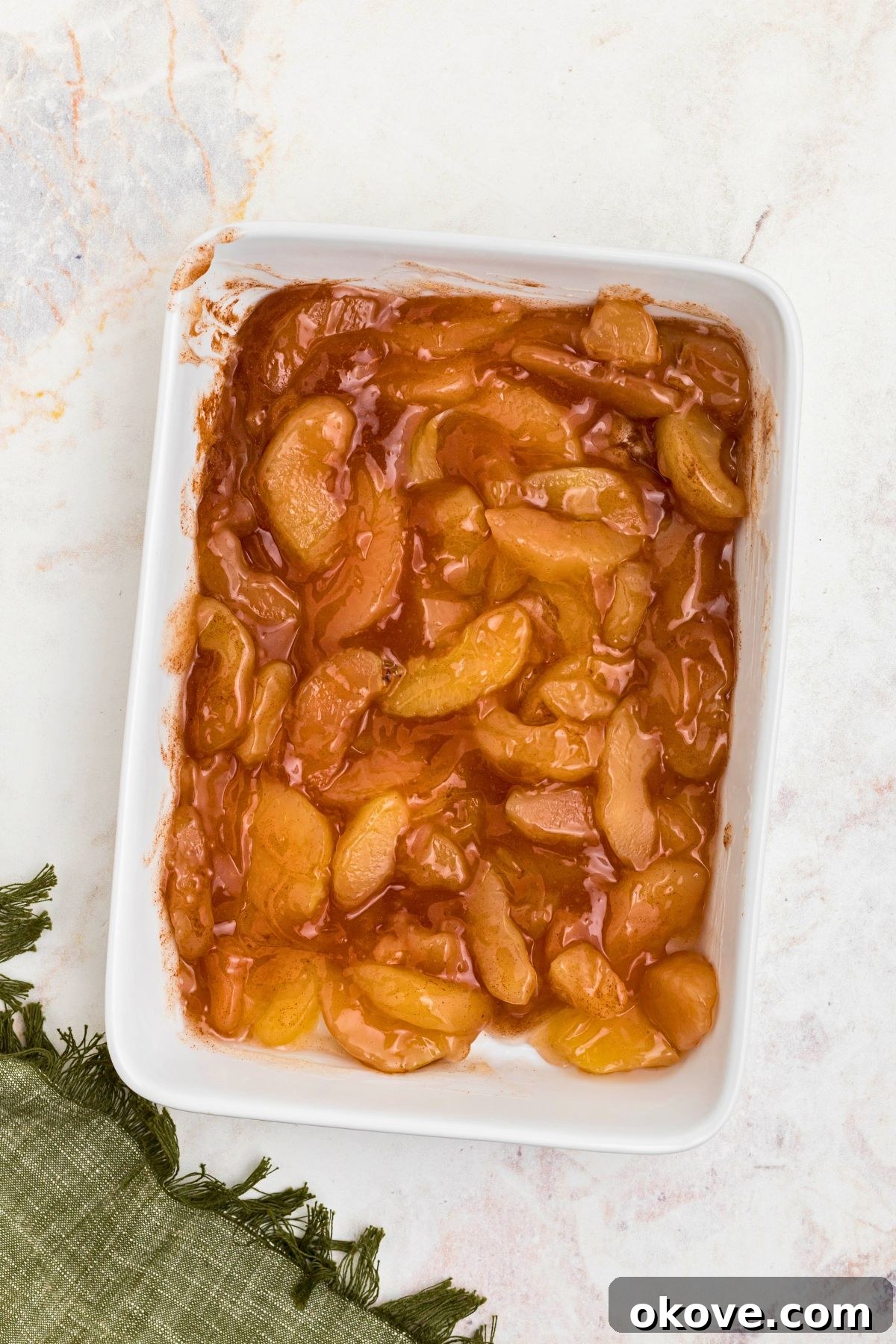 Apple pie filling and ground cinnamon mixed together in a white 9x13 baking dish.