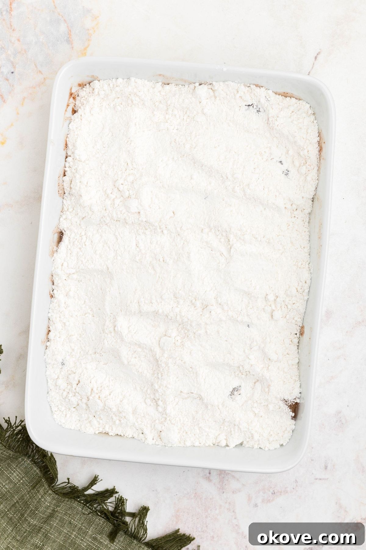 Yellow cake mix poured over pie filling in a white dish, without being stirred together.
