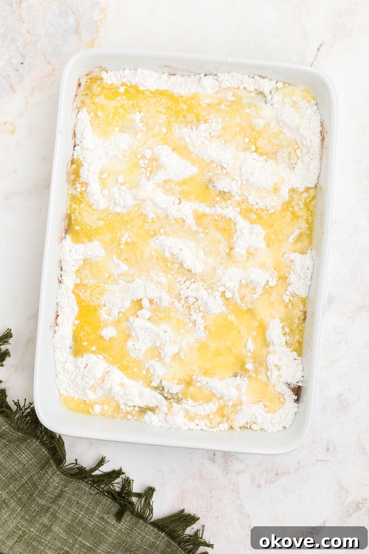 Melted butter drizzled on top of uncooked cake mix powder over apple pie filling in a white baking dish.