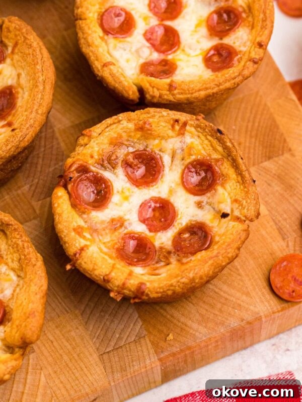 Golden-crusted pizza cupcakes on a wooden cutting board with pepperoni scattered around.