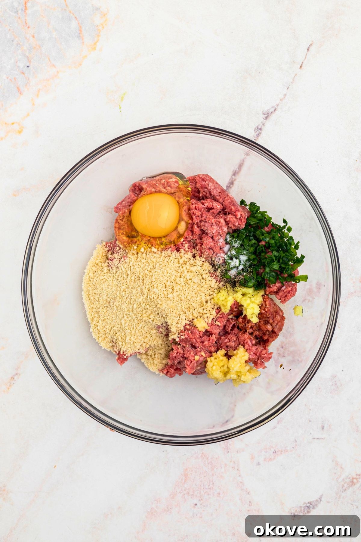 Ground beef, egg, breadcrumbs, ginger, garlic, and other ingredients, in a large mixing bowl before being mixed together.