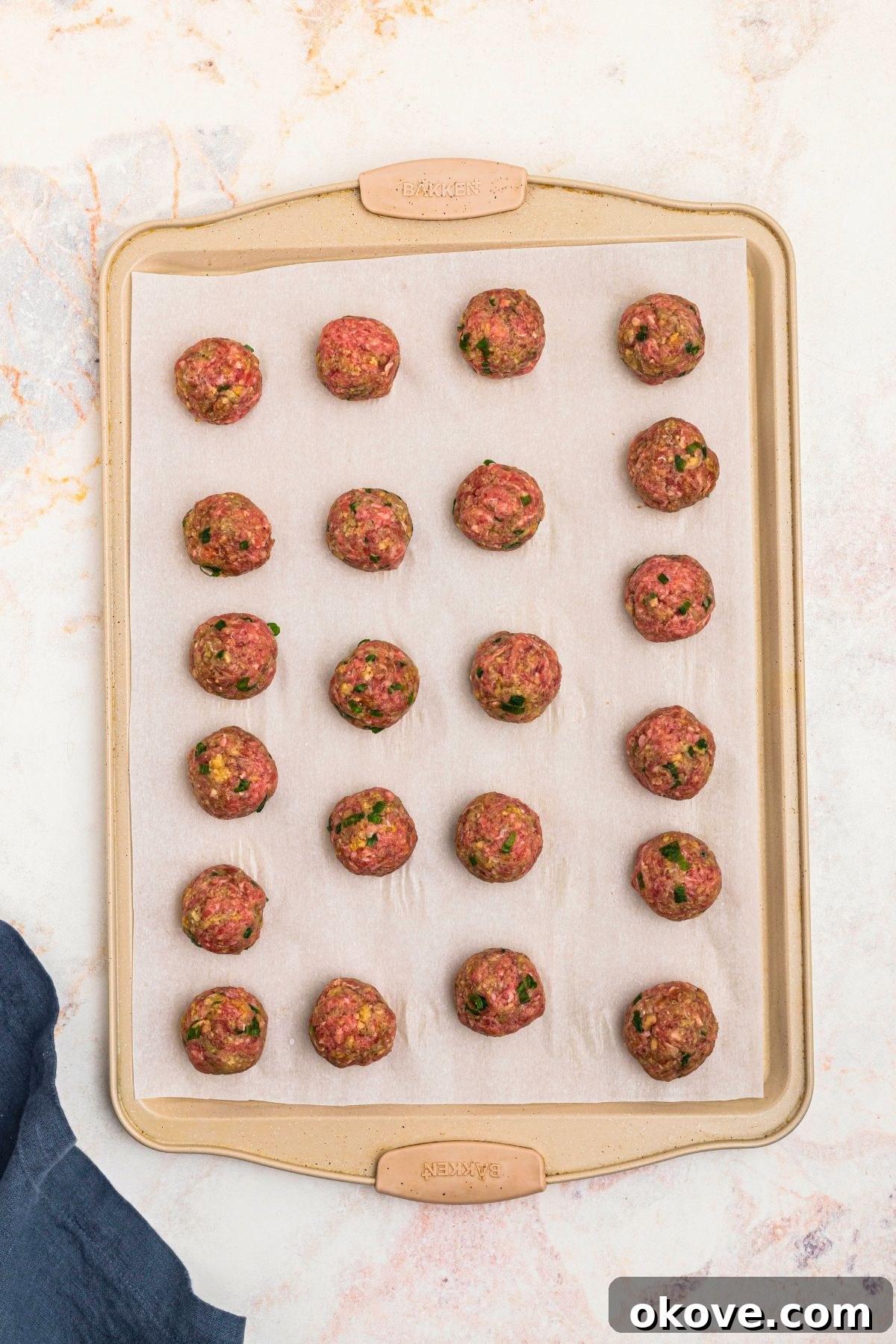Ground meat mixture, rolled into meatballs, placed on a baking sheet lined with parchment paper, before cooking.