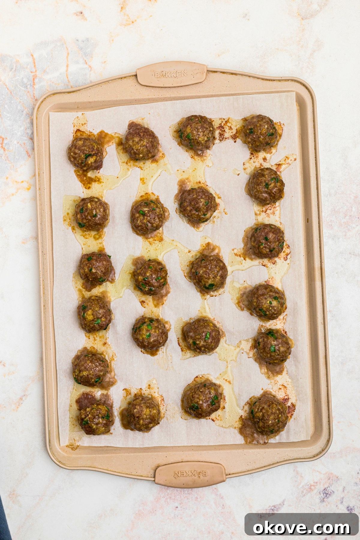 Baked meatballs on a parchment paper lined baking sheet.