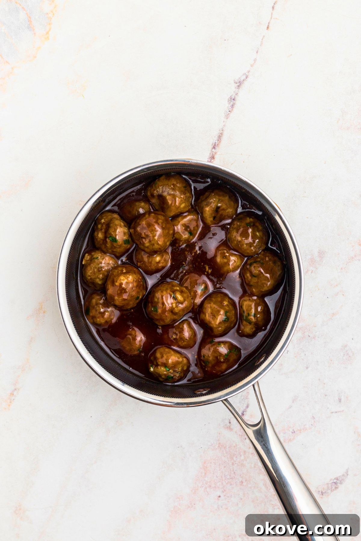 Cooked meatballs in a saucepan tossed with teriyaki sauce, on a marble table.