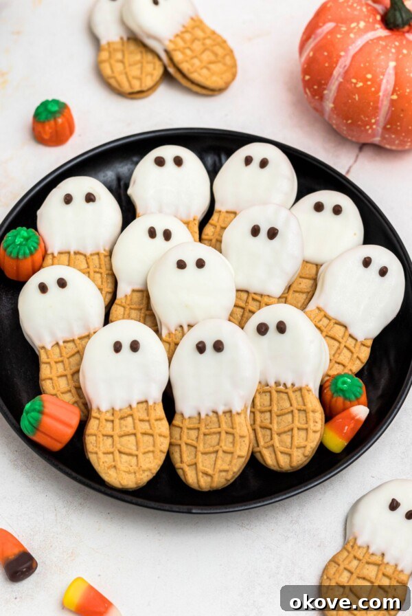 Spooky Halloween Chex Mix with Candy Corn and M&Ms 12 Black plate with peanut butter cookies dipped in white chocolate with chocolate dots for eyes, stacked together, on a marble table.