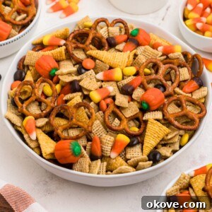 Spooky Halloween Chex Mix with Candy Corn and M&Ms 13 Large white bowl filled with Chex mix, pretzels, candy corn, and candies, with some scattered around the table.
