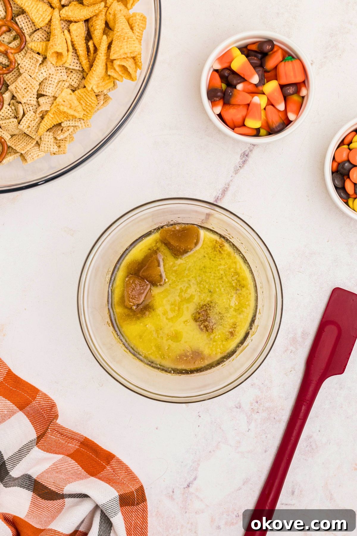 Spooky Halloween Chex Mix with Candy Corn and M&Ms 5 Butter and brown sugar melted together in a clear glass bowl on a marble table.
