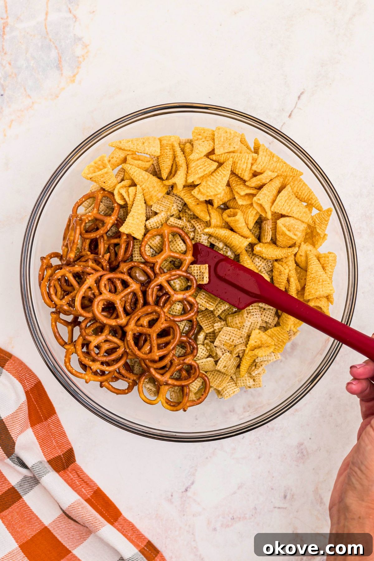 Spooky Halloween Chex Mix with Candy Corn and M&Ms 6 Melted butter and brown sugar mixed with cereal, pretzels, and bugle chips, in a large clear glass mixing bowl.