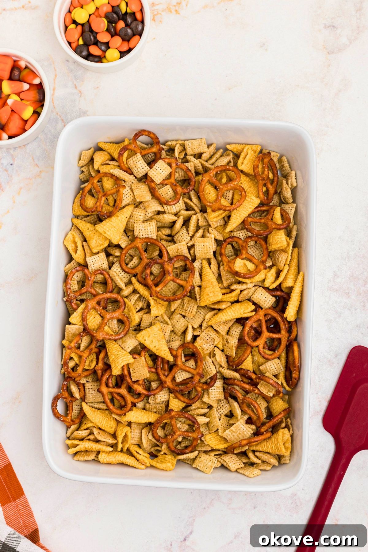 Spooky Halloween Chex Mix with Candy Corn and M&Ms 7 Chex mix ingredients mixed together in a 9x11 baking dish before being baked together.