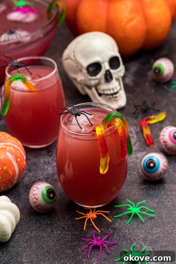 Spooky Halloween Chex Mix with Candy Corn and M&Ms 10 Glass of Halloween Punch in with gummy worms hanging over the side of the glass, in front of plastic skull and spiders.
