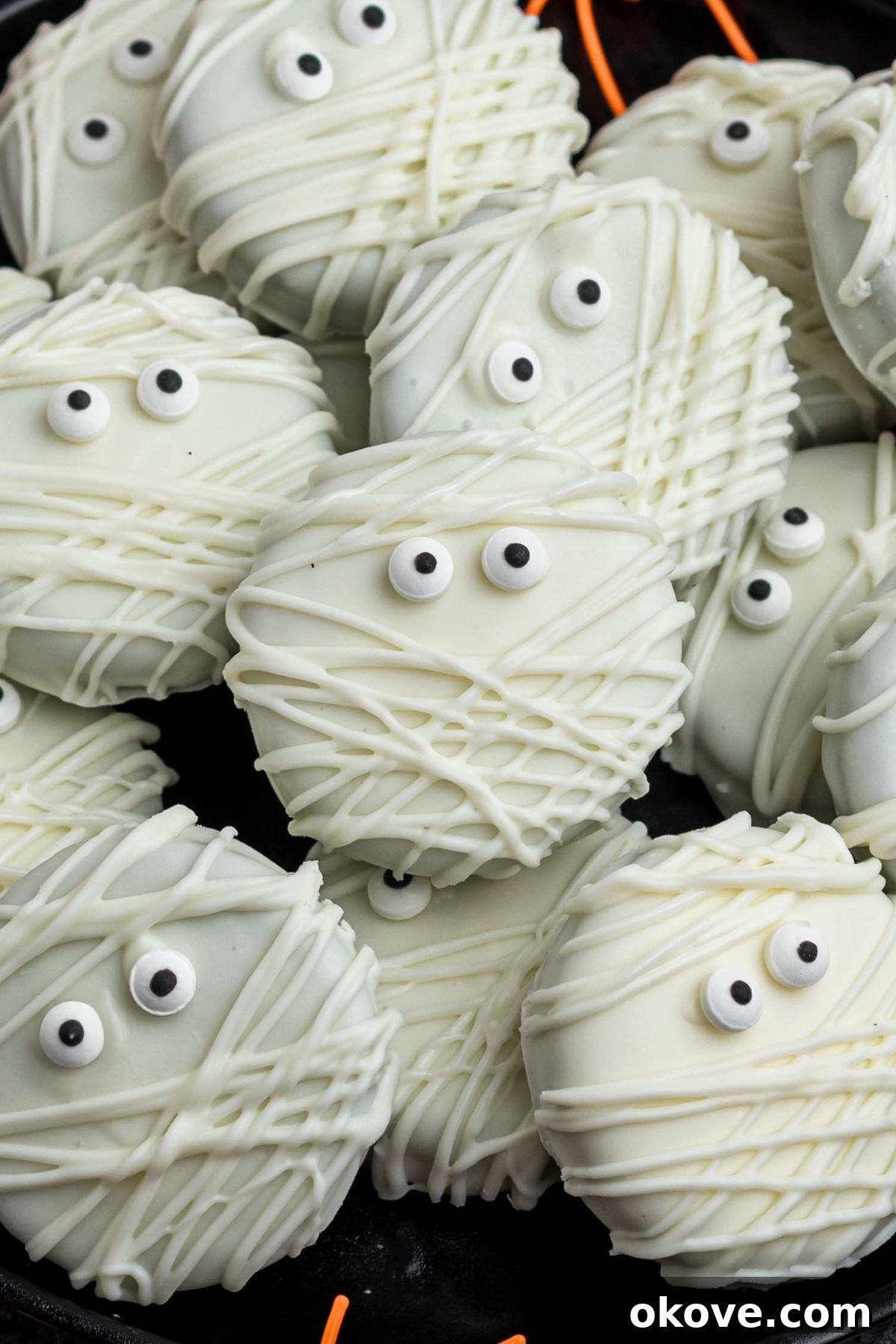 Oreo cookies, dipped and drizzled in white chocolate, with candy eyes, on a black plate, with orange spiders as decoration, on a black marble table.