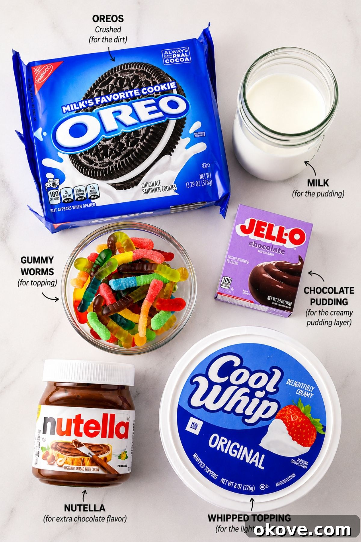 Oreos, cool whip, glass of milk, bowl of gummy worms, and a tub of Nutella, on a white marble table.