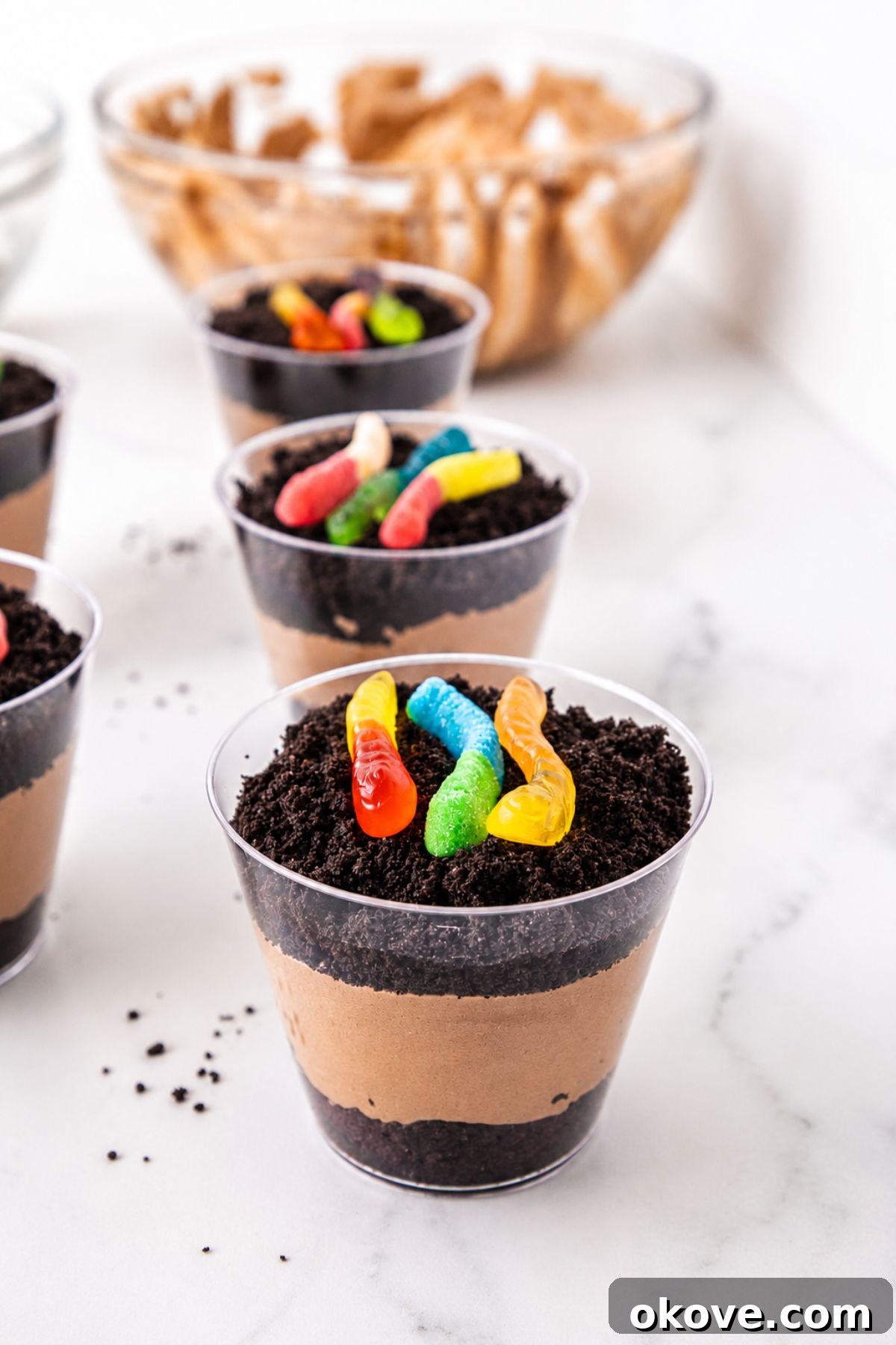 Individual cups filled with layers of crushed cookies, pudding, and then topped with gummy worms.