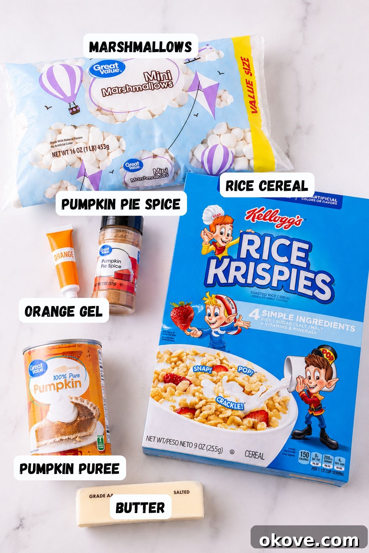 Ingredients needed to make rice krispies, along with pumpkin filling and spice, on a white marble table.