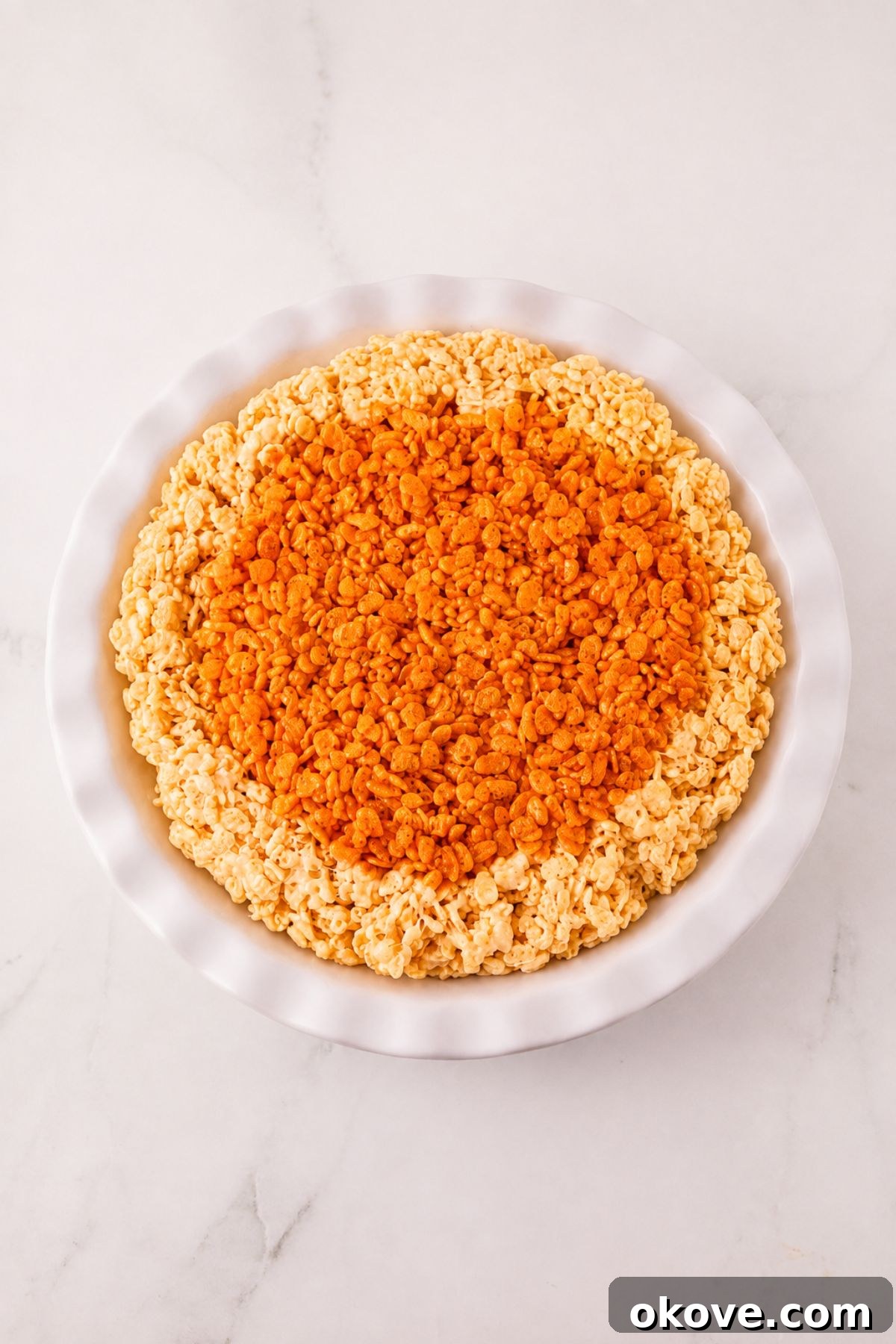 Whole pie of krispie treats in a pie plate, before cutting, on a marble table.