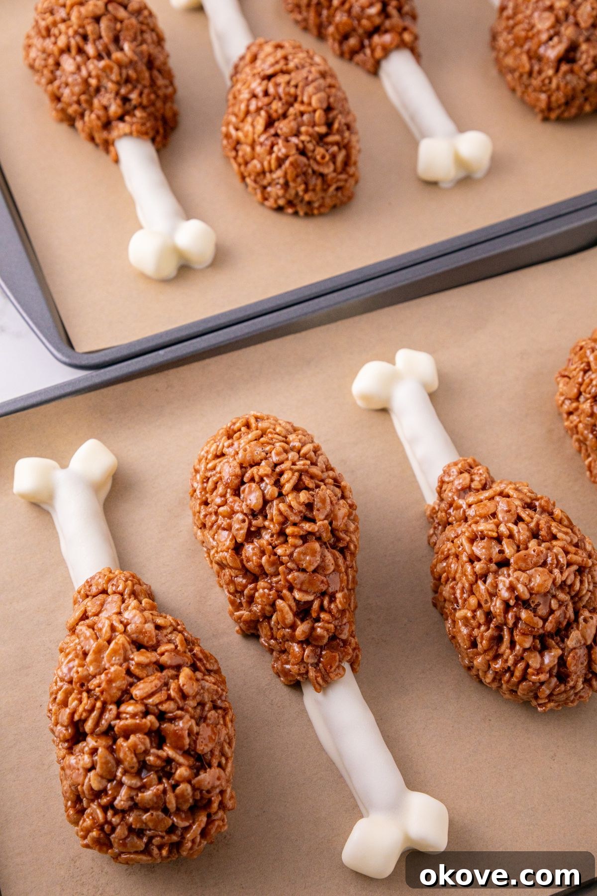 Dipped pretzels, with cocoa krispies, shaped into drumsticks, on a parchment paper lined baking sheet.