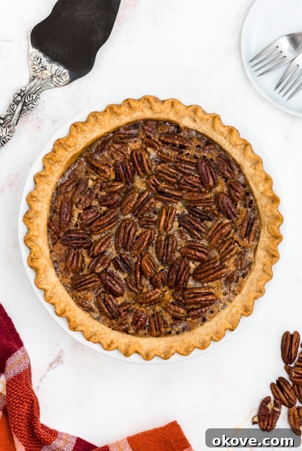 Pecan pie with golden fluted crust on a marble table with spatula and pecans on the table.