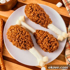 Cocoa krispie treats shaped around white chocolate dipped pretzel rods and marshmallow tips to look like turkey drumsticks. On a white plate, set on wooden cutting board, with marshmallows scattered around.