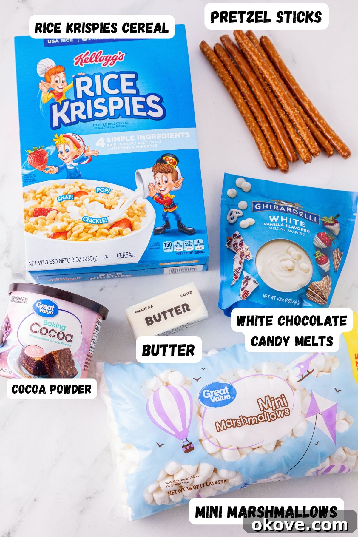 Rice Krispie cereal, cocoa powder, pretzels, marshmallows, butter, and melting chocolates, labeled on a white marble table. 