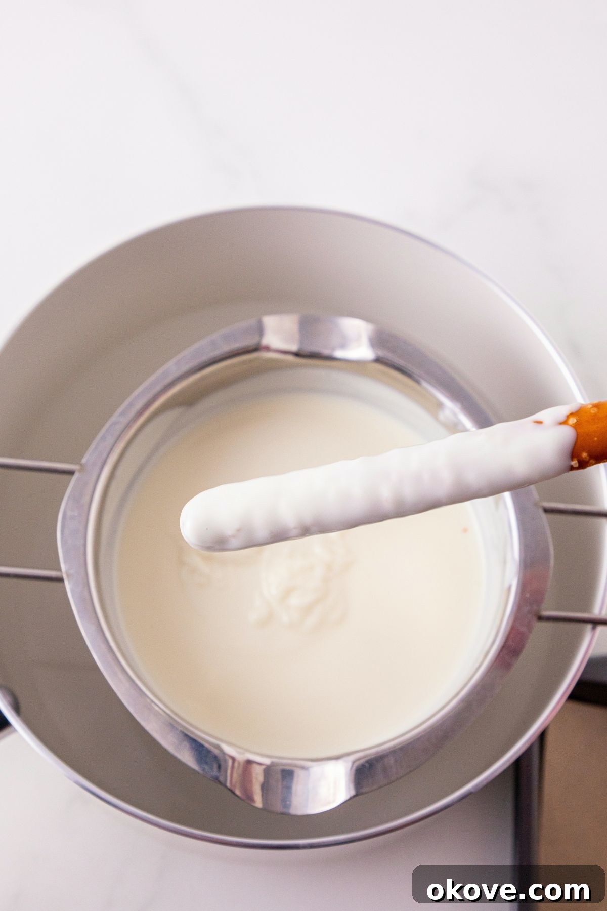 White chocolate melts, melted in a pan, and stirred until smooth and creamy, with a pretzel rod being dipped into the melted coating.