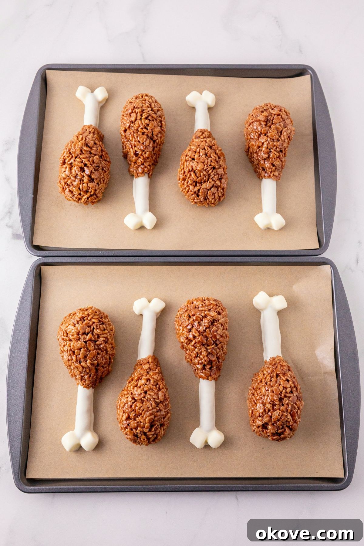 Dipped pretzels, with cocoa krispies, shaped into drumsticks, on a parchment paper lined baking sheet. 