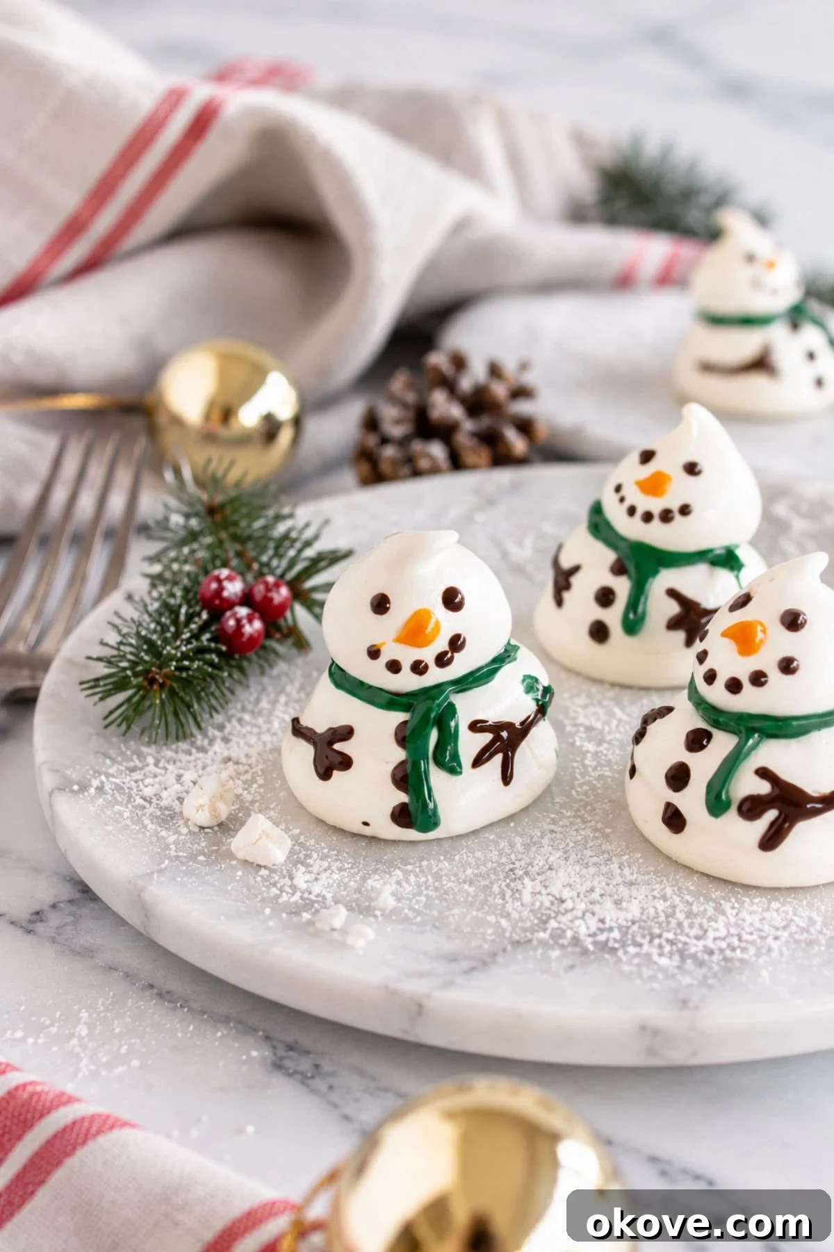 White meringue snowmen on a white plate with holiday decorations around the table. 