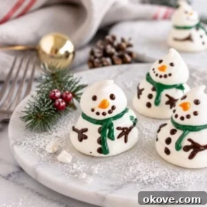 White meringue snowmen on a white plate with holiday decorations around the table.
