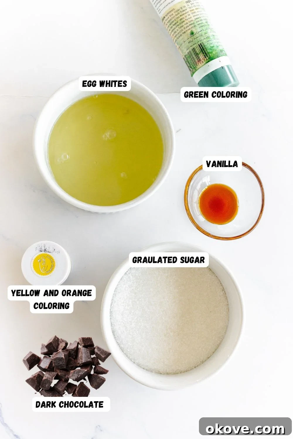 Ingredients needed to make snowman meringues measured into small bowls and labeled on a marble table. 