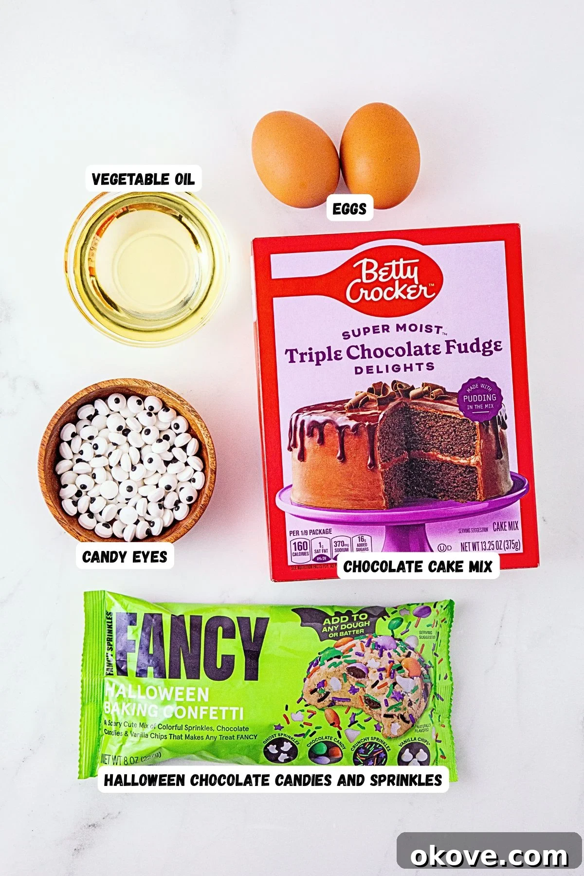 Ingredients needed to make monster cake mix cookies on a white marble table, labeled. 