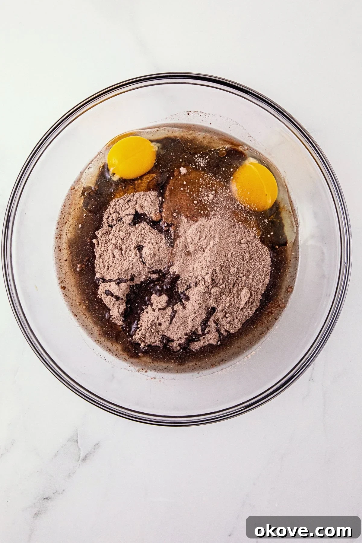 Chocolate cake mix, eggs, and oil, in a large clear glass mixing bowl. 