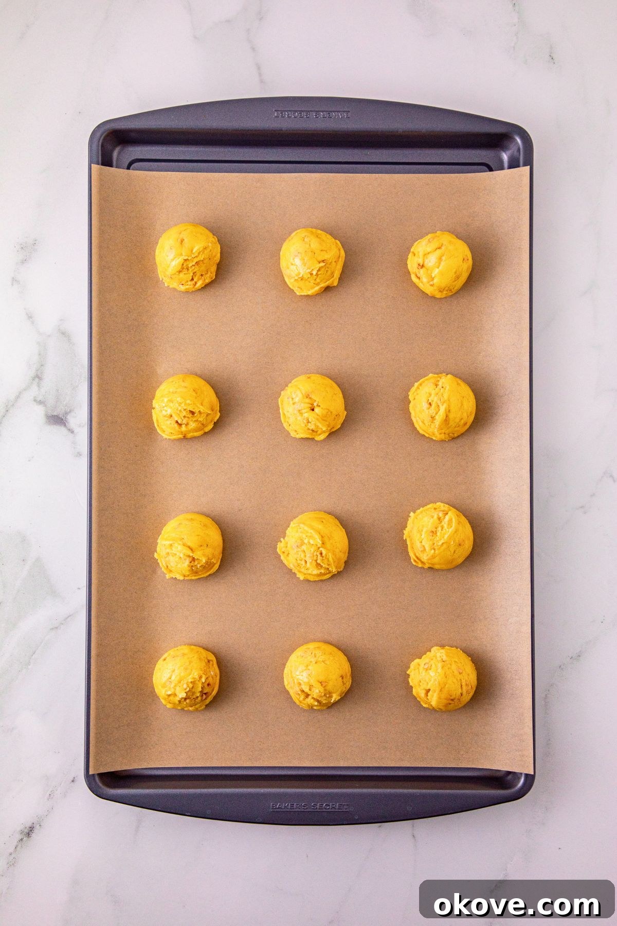 Scoops of dough on a baking sheet, lined with parchment paper. 