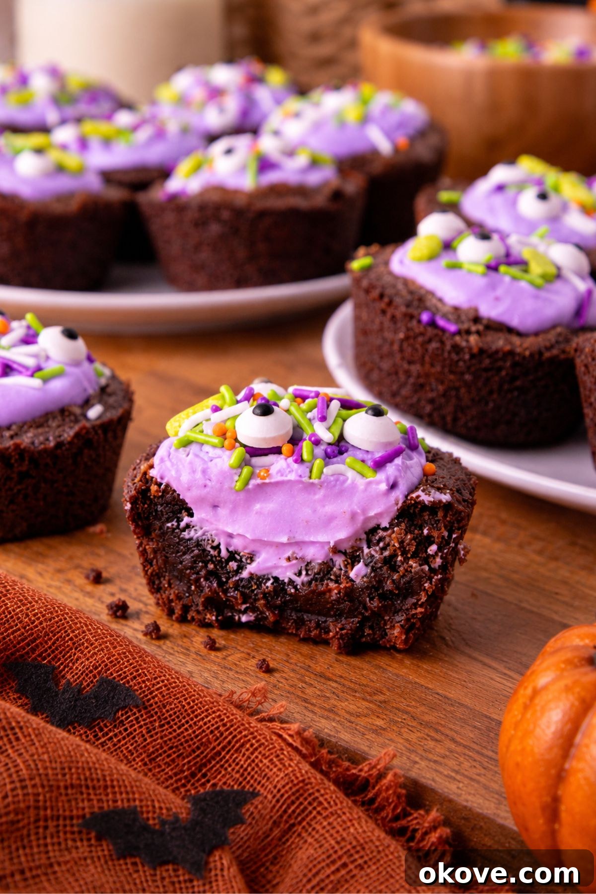 Brownie bites filled with purple frosting and topped with Halloween sprinkles, on a wooden board. 