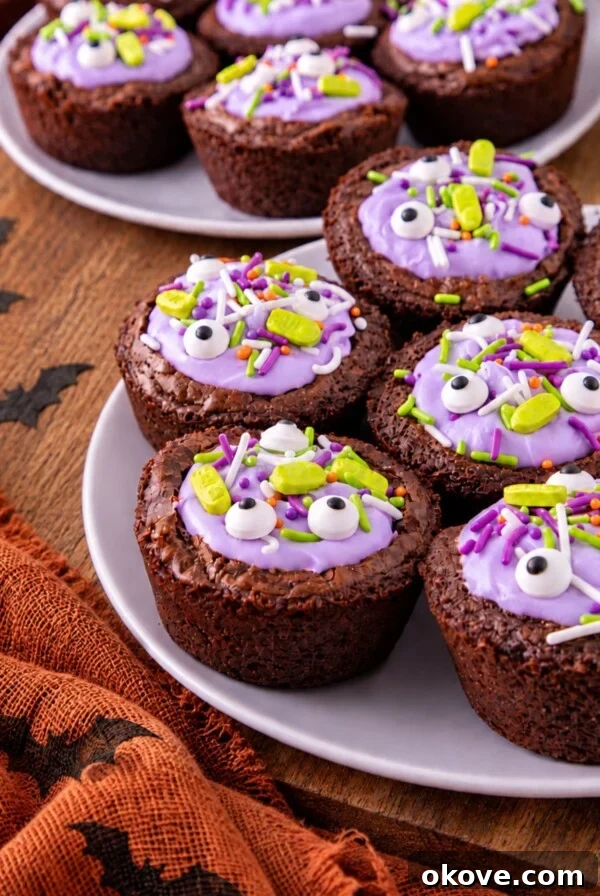 Brownies topped with purple frosting and Halloween sprinkles on a white plate with an orange linen on a wooden board.