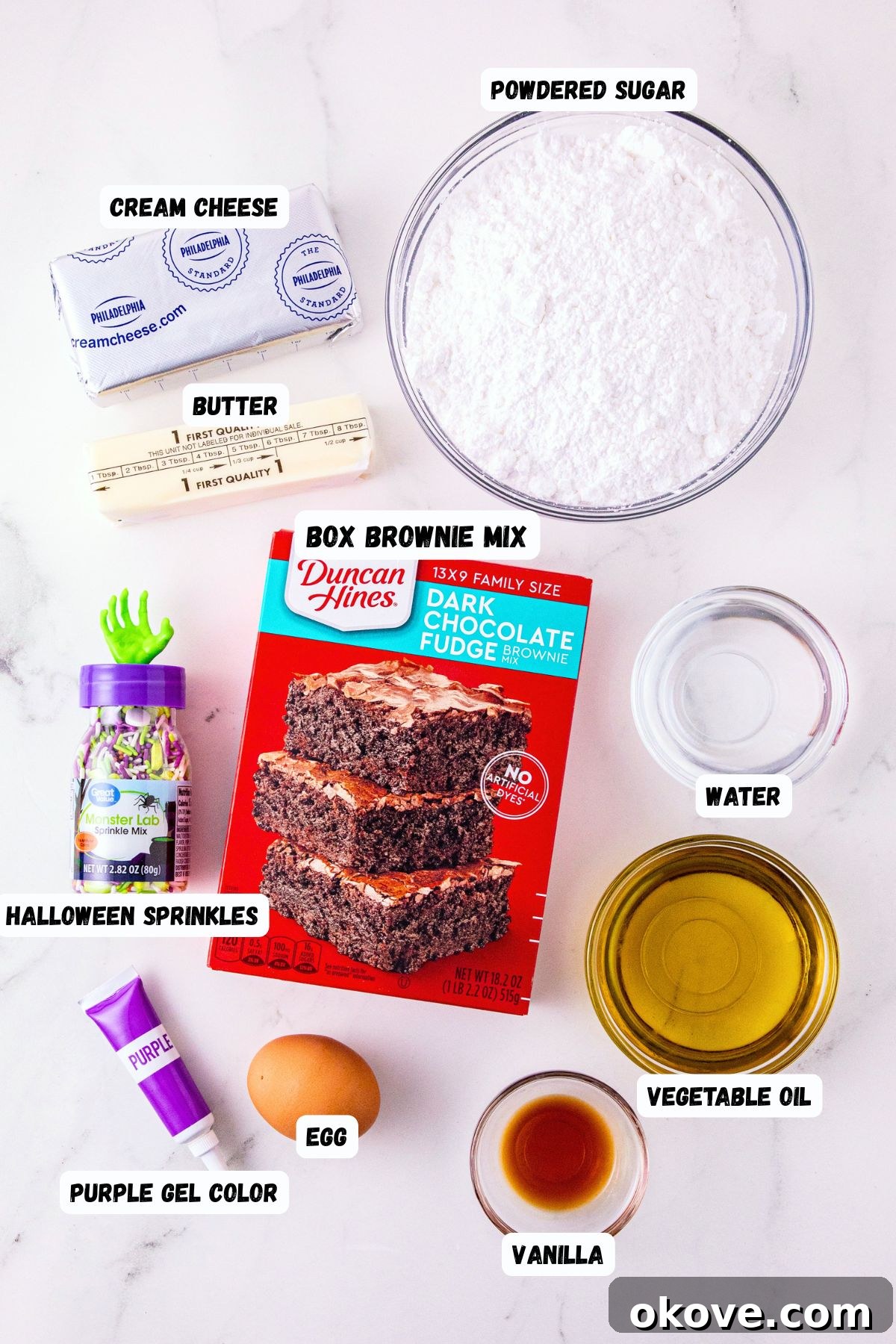 Ingredients of brownie mix, egg, cream cheese, powdered sugar, butter,  coloring, vanilla, water, oil, and sprinkles, measured and labeled on a marble table. 