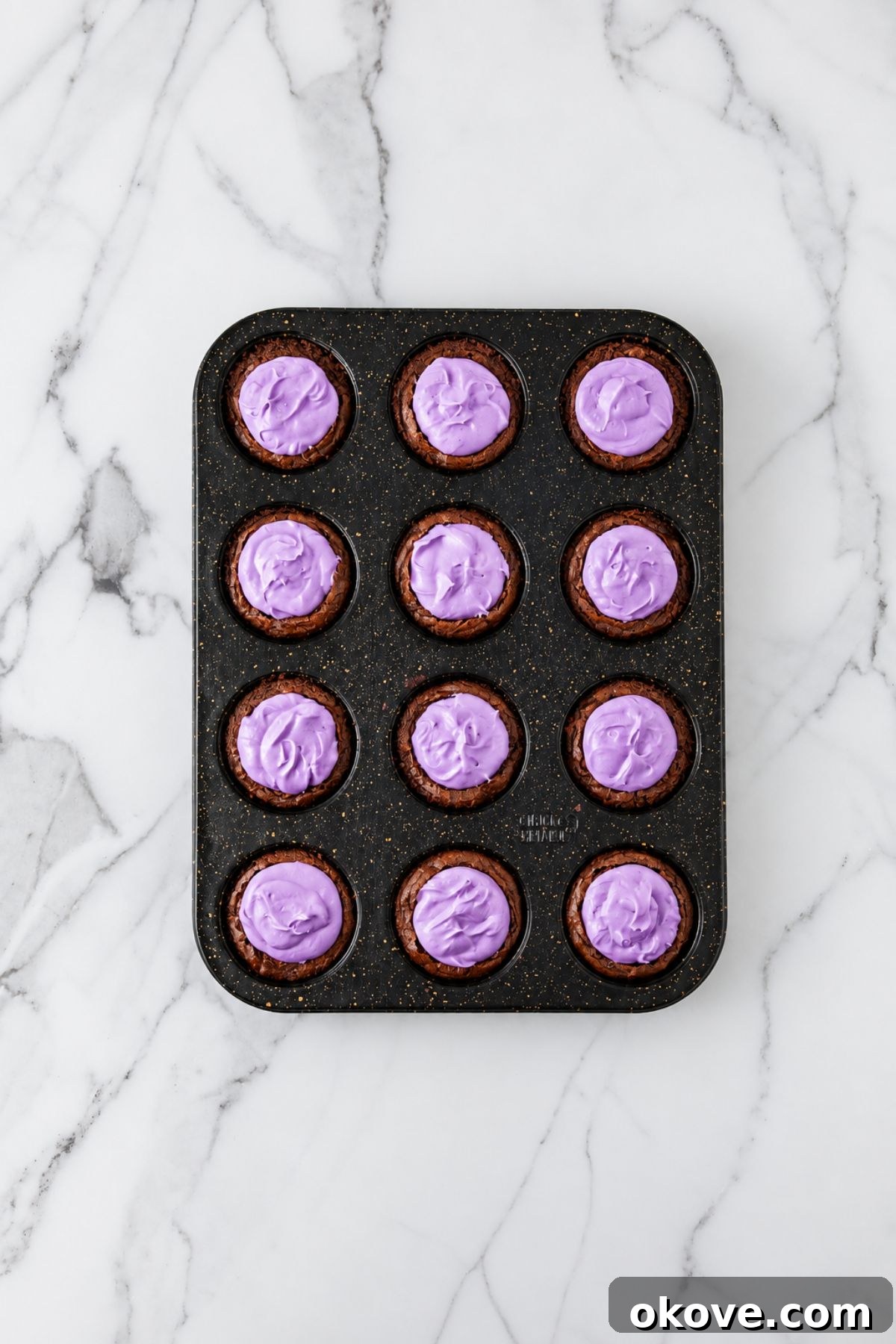 Brownie bites filled with purple frosting in a muffin pan. 